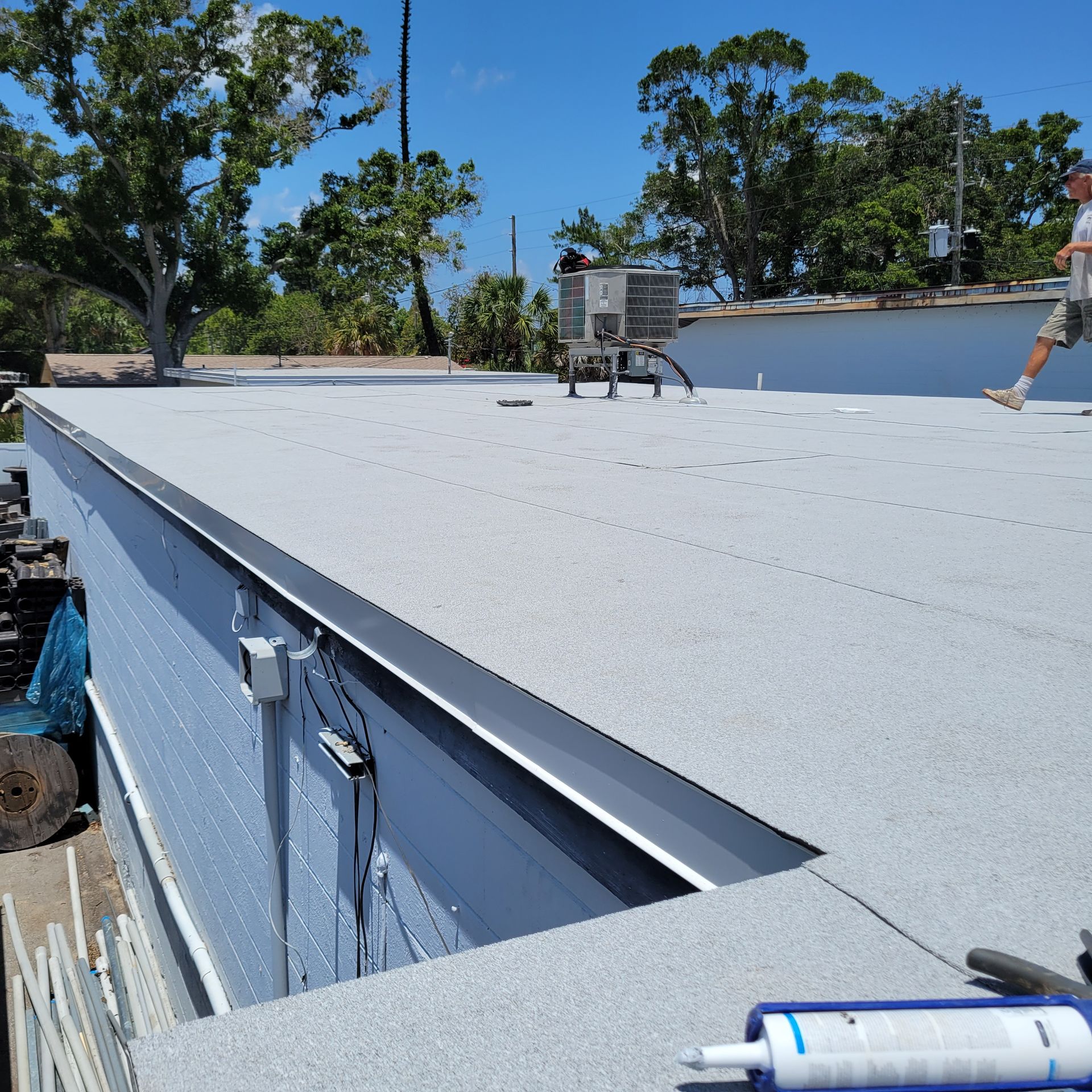A new flat roof membrane installed by Reliant Service Team, against blue sky and live oaks