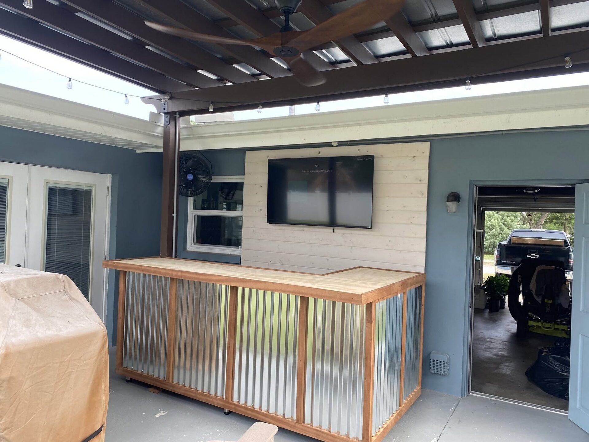A pergola outdoor kitchen with a corrugated-metal bar, built by Reliant Service Team