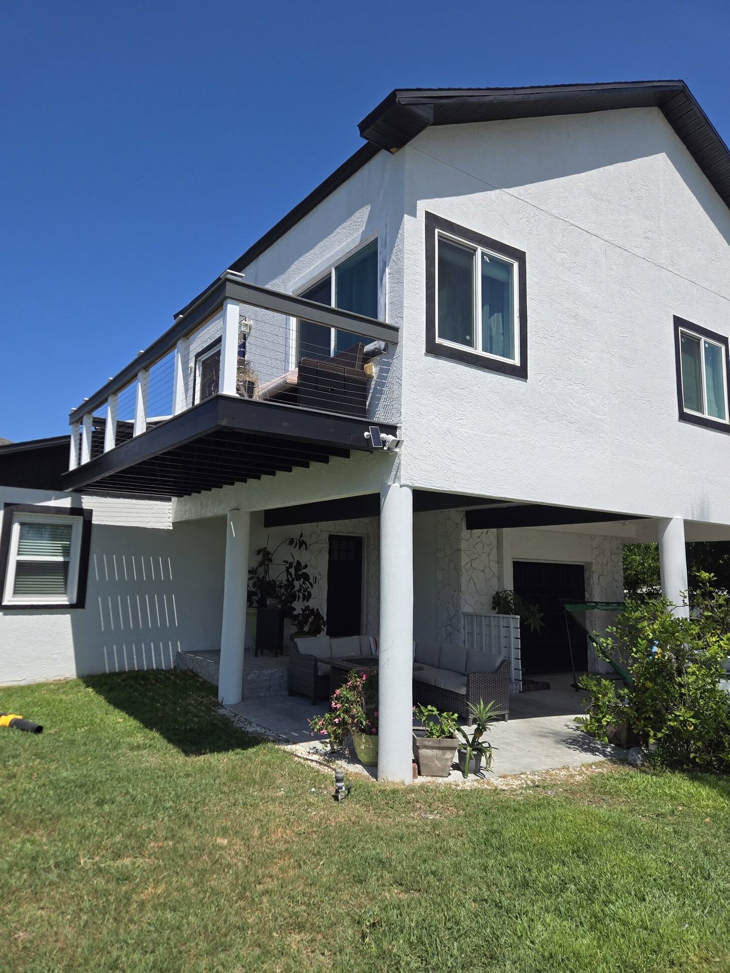 A raised white-stucco two-story coastal home with a cable-rail balcony, built by Reliant Service Team
